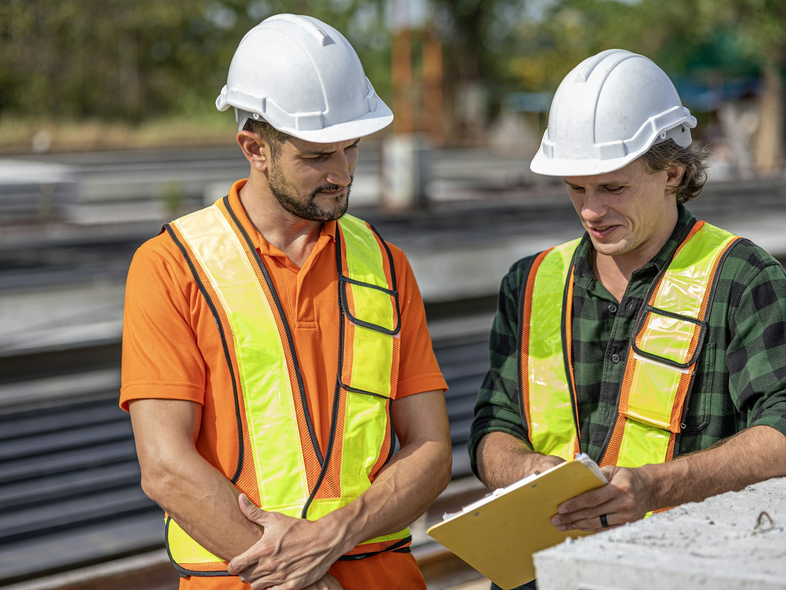 Two site leads in hard hats and high-visibility vests checking a clipboard together